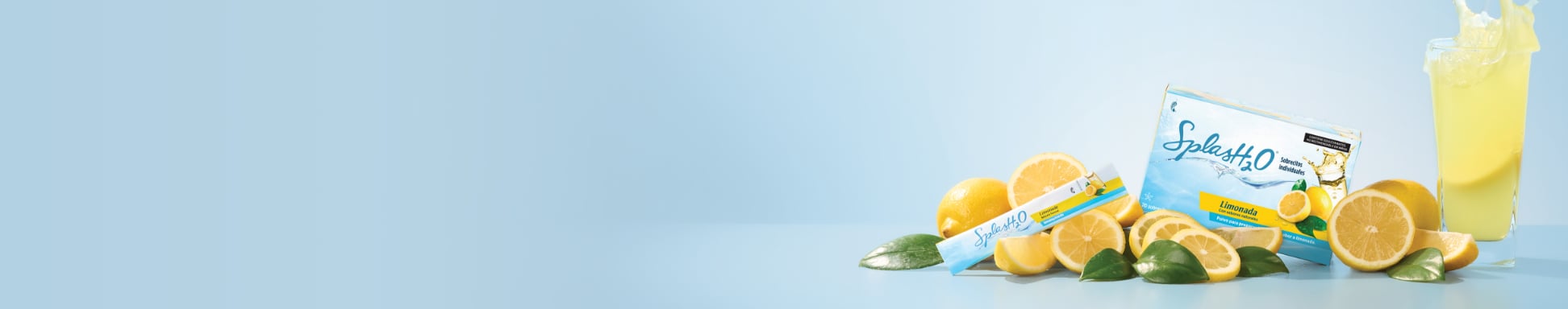 Una caja y un sobre de SplashH2O sabor limonada se encuentran entre limones frescos y hojas verdes sobre un fondo azul claro, transmitiendo una temática cítrica y refrescante.