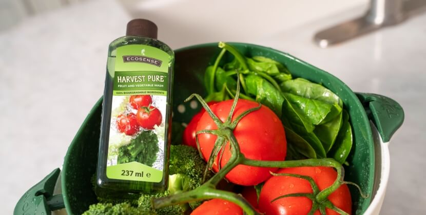A bottle of Harvest Pure in a strainer bowl with some tomatoes and broccoli.