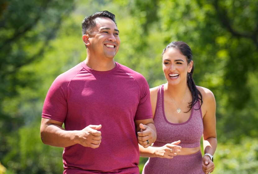 A smiling man and woman jogging side by side in athletic clothing.
