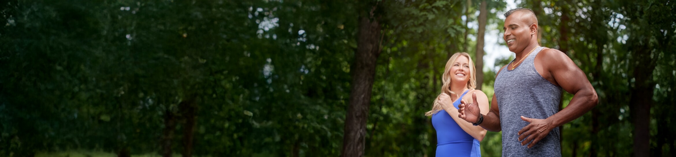 A man and woman jogging through a forest.
