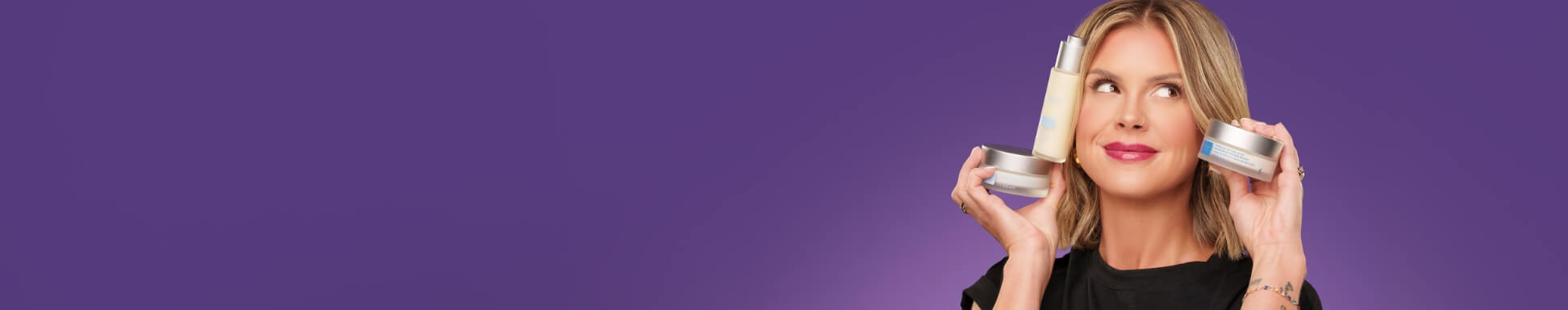 Mujer con una blusa negra y productos de cuidado facial cerca de su rostro sobre un fondo morado.