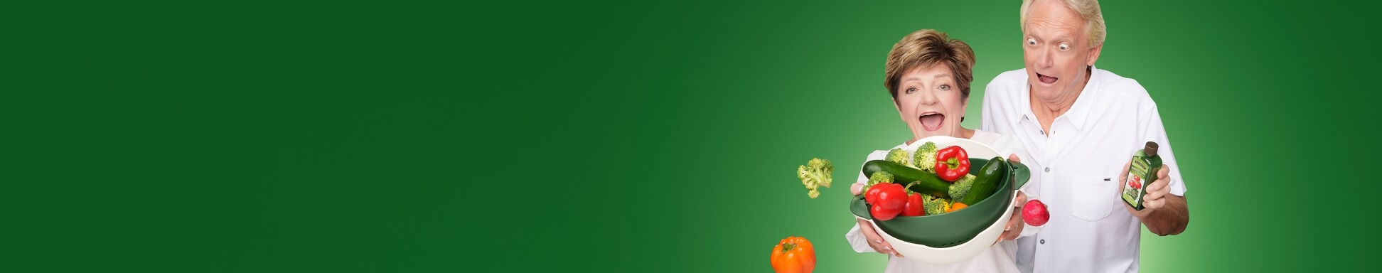 A surprised elderly couple holds a bowl of fresh vegetables, including bell peppers and broccoli. The man holds a bottle labelled "Harvest Pure™ Fruit And Vegetable Wash" against a green backdrop.
