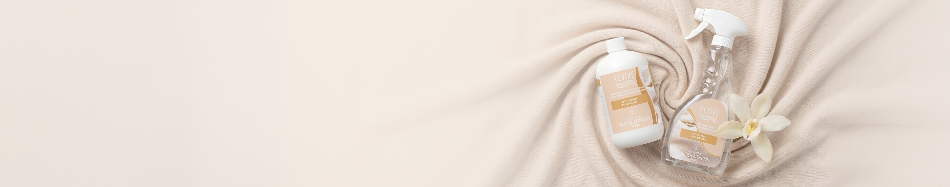 Two Revive cleaning products, a bottle and spray, on a soft beige fabric with a white orchid. The scene conveys freshness and elegance.