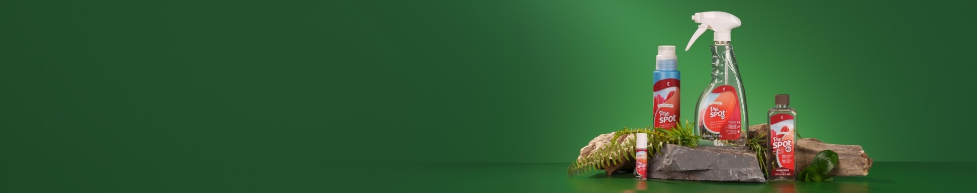 A collection of cleaning products labeled "Pre Spot" are displayed on rocks and wood against a green background. The setup conveys a natural, eco-friendly theme.