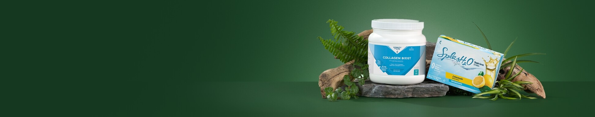 Collagen Boost and Splash H2O Lemonade sit on a stone, surrounded by driftwood and green leaves, against a dark green background.