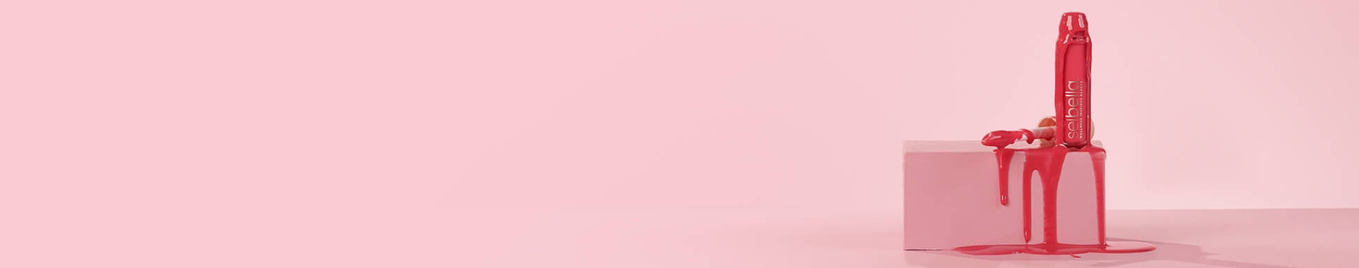 Sei bella lip oil dripping down the tube and over a pink box on a pink backdrop
