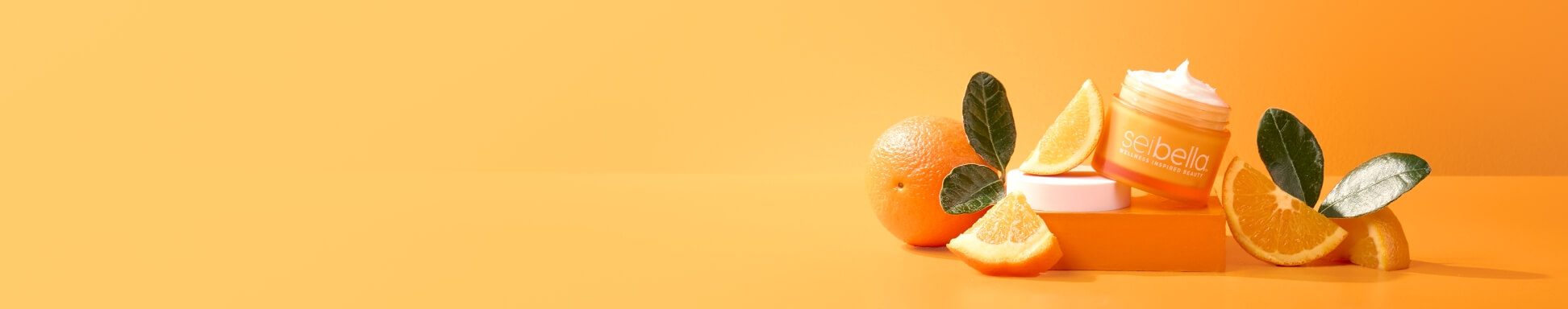 Vitamin c daily defense cream open on a orange box surrounded by oranges and leaves on an orange backdrop