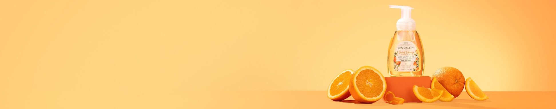 A bottle of Sun Valley Sweet Orange soap on a peach background, surrounded by fresh orange halves and slices, conveying a refreshing citrus vibe.