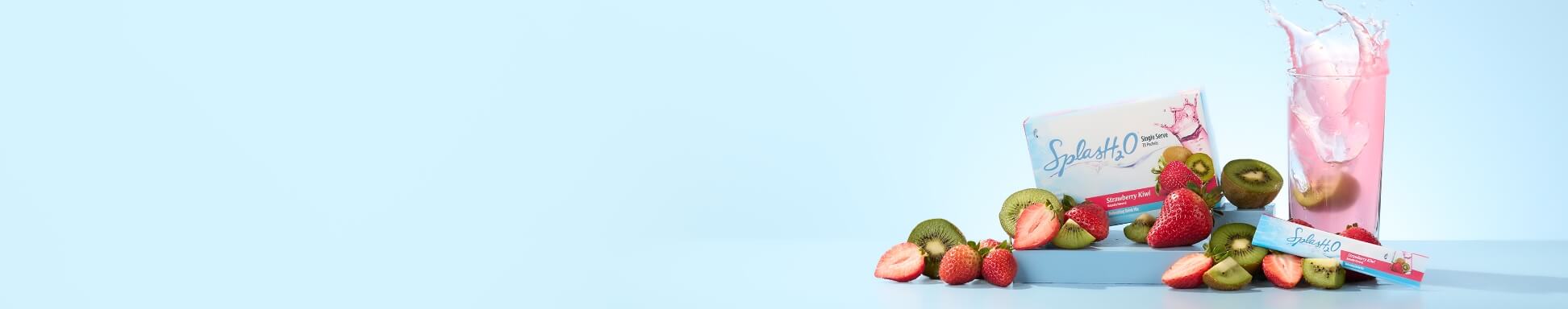 A box and a packet of SplasH2O next to an overflowing tall glass, surrounded by fresh strawberries and kiwis.