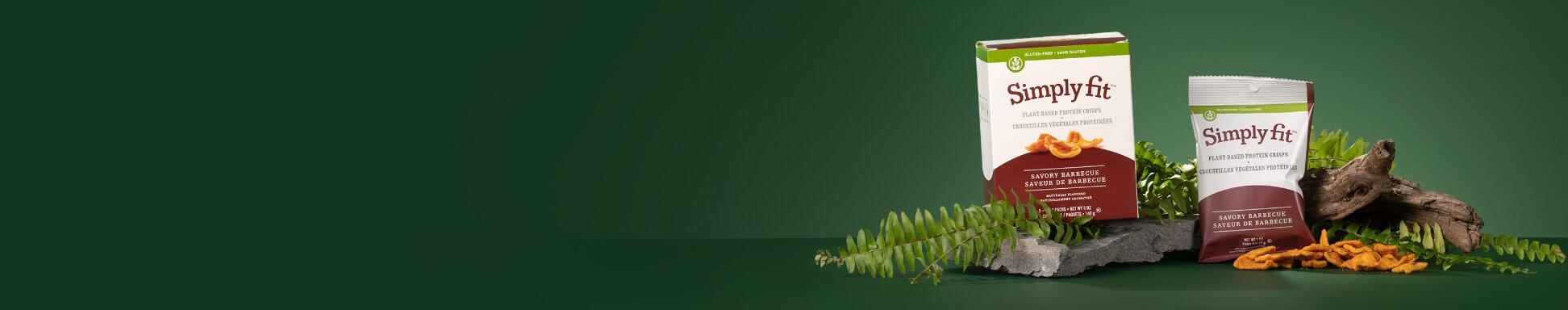 Two Simply Fit supplement packages stand among fern leaves, rocks, and orange botanicals against a dark green background.