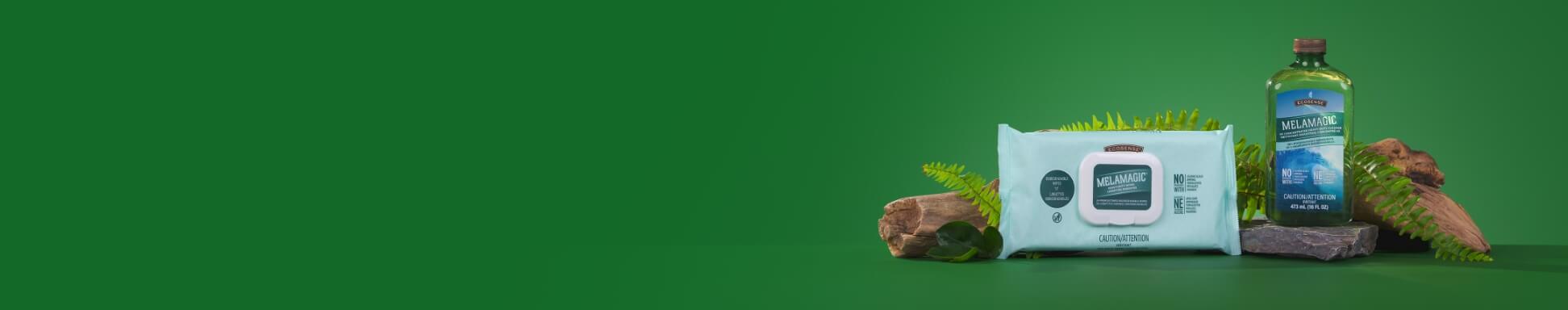 MelaMagic Wipes and MelaMagic Heavy-Duty Cleaner in a green bottle and white wipes, displayed on rocks with ferns against a vivid green background.