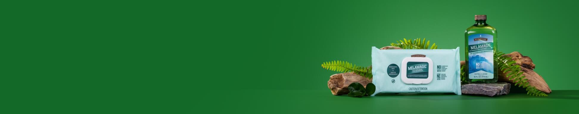 MelaMagic Wipes and MelaMagic Heavy-Duty Cleaner in a green bottle and white wipes, displayed on rocks with ferns against a vivid green background.