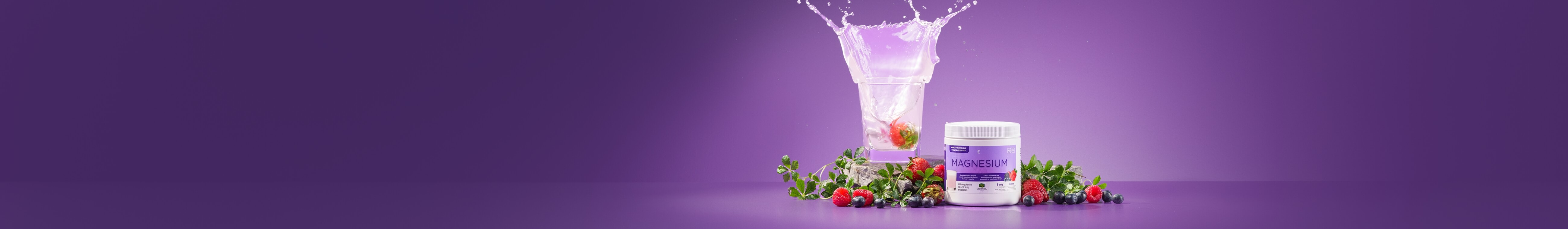 A magnesium supplement jar on a purple background, surrounded by fresh berries and leaves. A clear glass with splashing water and berries adds liveliness.