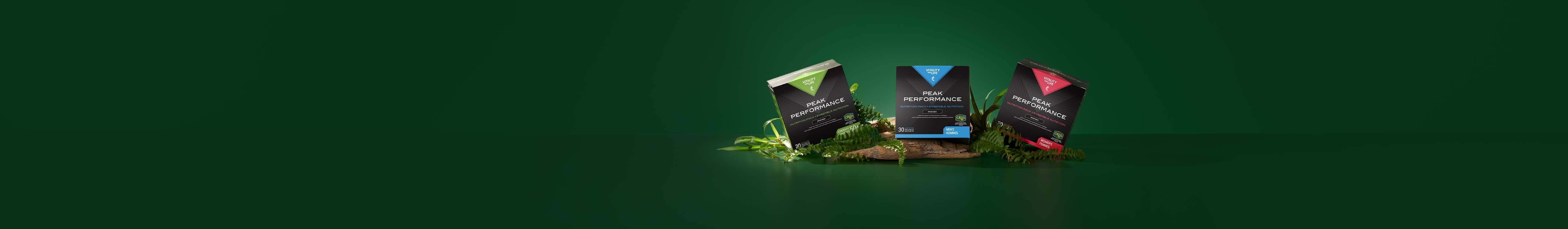 Three Peak Performance supplement boxes in black, green, and red stand on moss and driftwood against a dark green background.