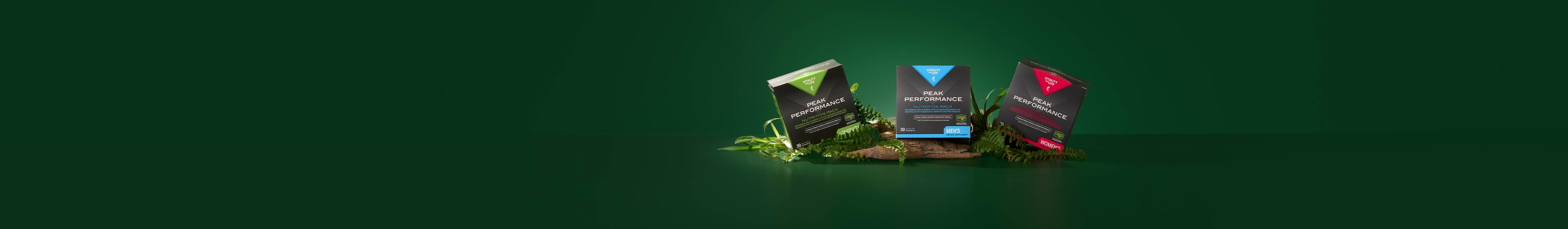 Three Peak Performance supplement boxes in black, green, and red stand on moss and driftwood against a dark green background.