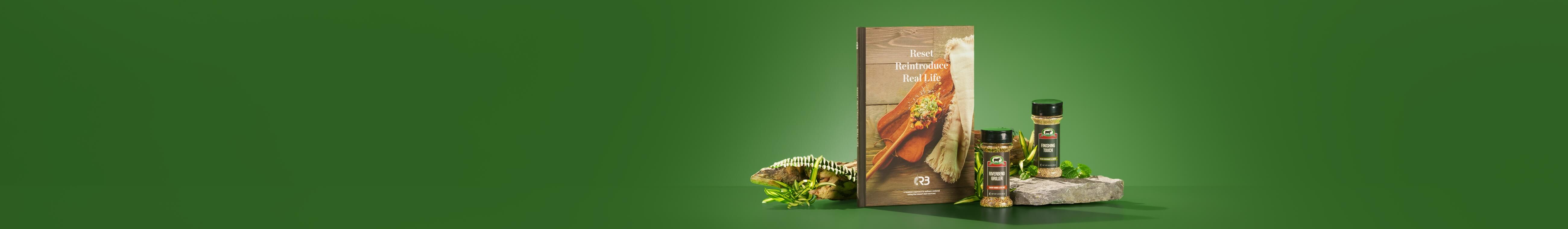 The R3 Cookbook and Spices Bundle surrounded by green ferns, a wooden log, and a slab of stone.