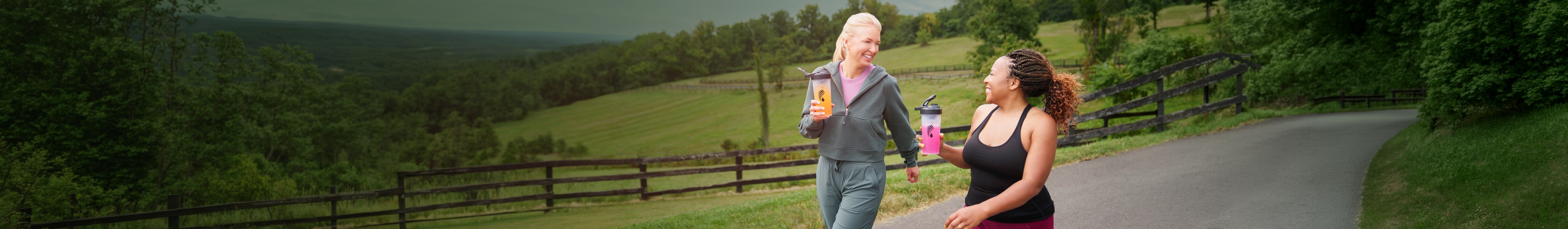 Two women walking together, each holding a blender bottle filled with a beverage.